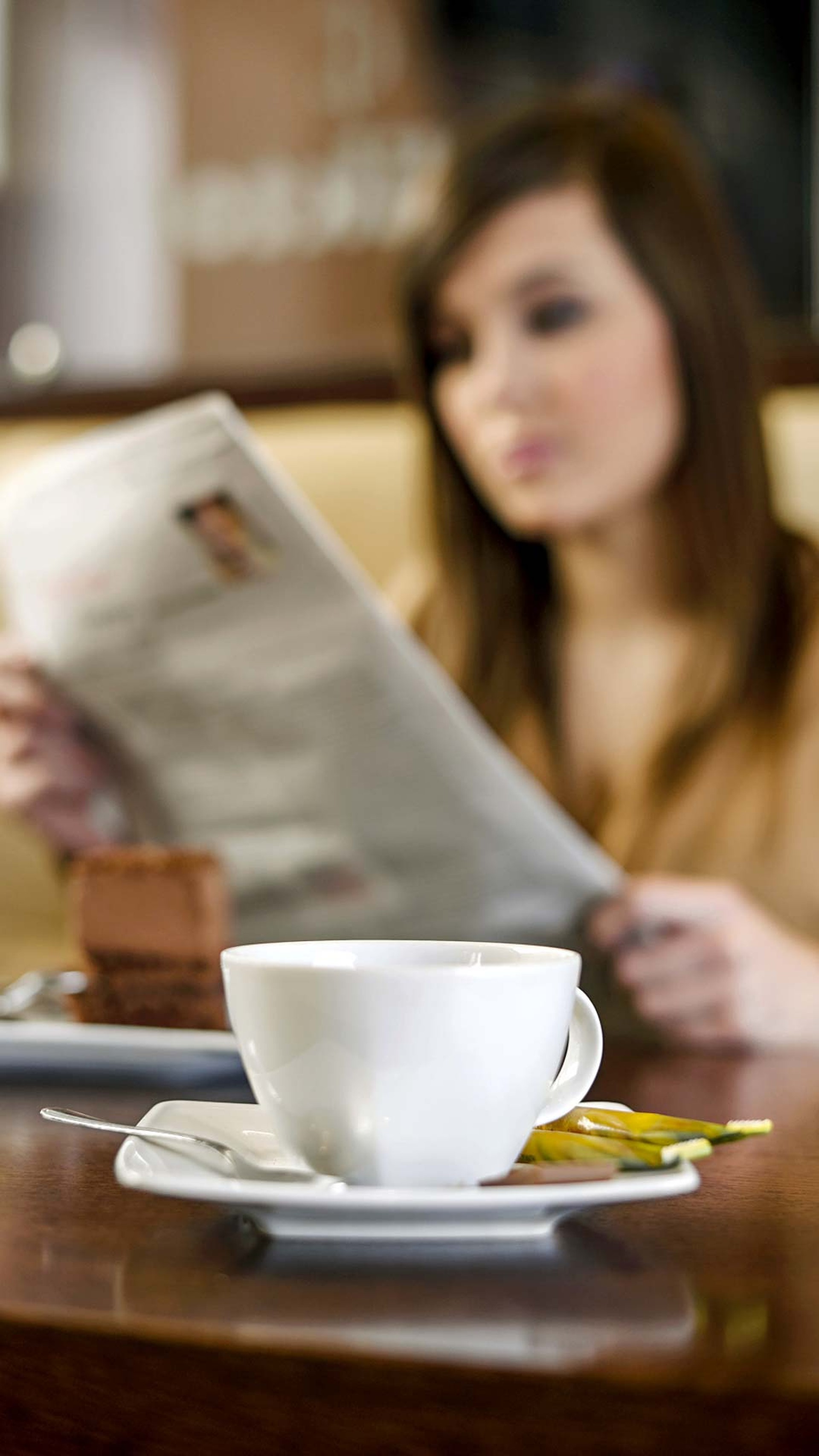 Frau sitzt am Tisch und liest Zeitung